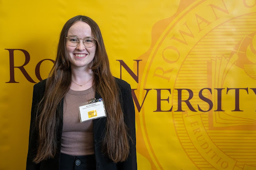 The woman smiles in a formal portrait against a yellow university backdrop.