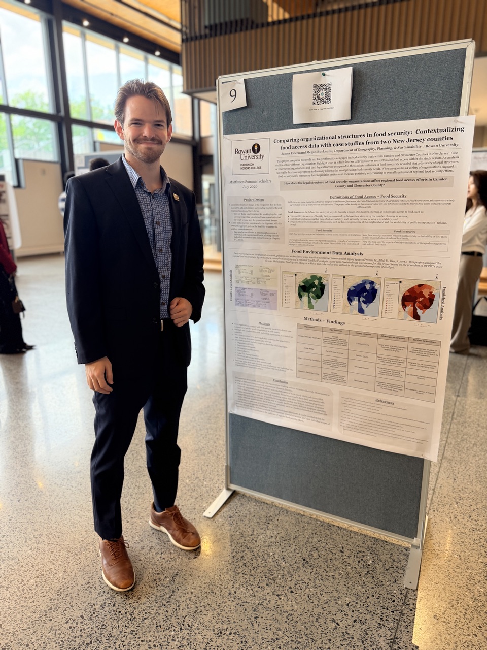 James Flocco, a Martinson Summer Scholar in a dark suit, smiling next to his research poster titled "Comparing organizational structures in food security."