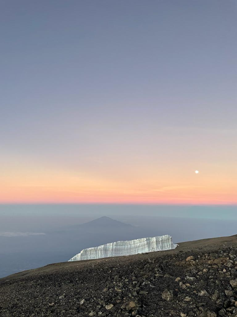 Mt Meru in the background of some of the last remaining glacier ice on the summit of Kilimanjaro at sunrise with the moon still in view.
