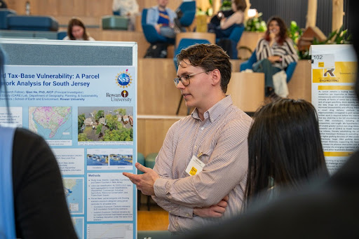 A man in a striped shirt gestures toward his South Jersey land tax research poster.