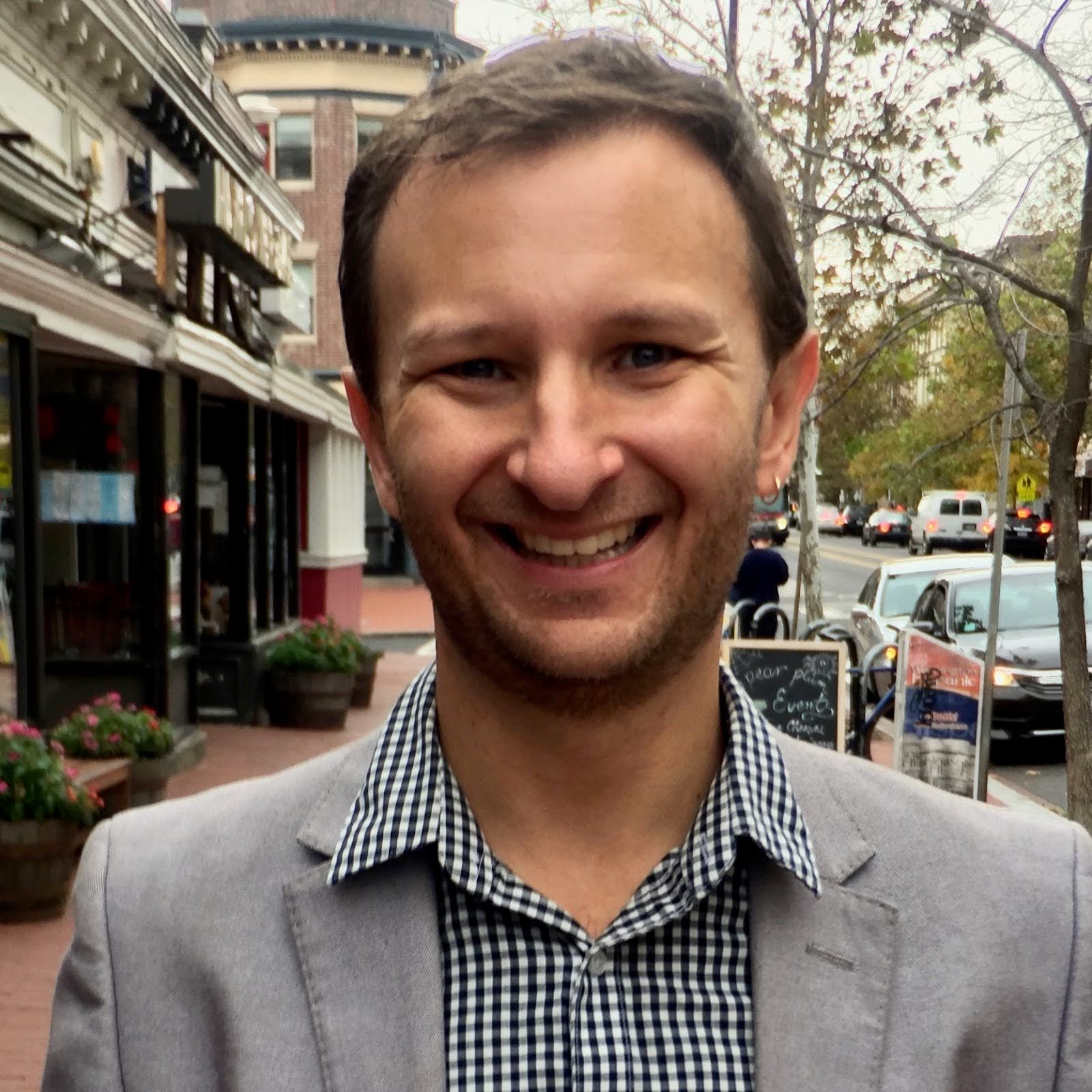 Close up shot of Dr. Lou Thomas wearing checkered button up shirt and a grey blazer on a brick sidewalk in a downtown area