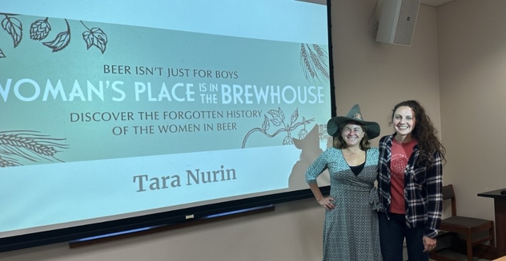 Dr. Ashley York stands with Author Tara Nurin wearing a witch hat while she talks about the historical relationship between witches and women brewing beer.